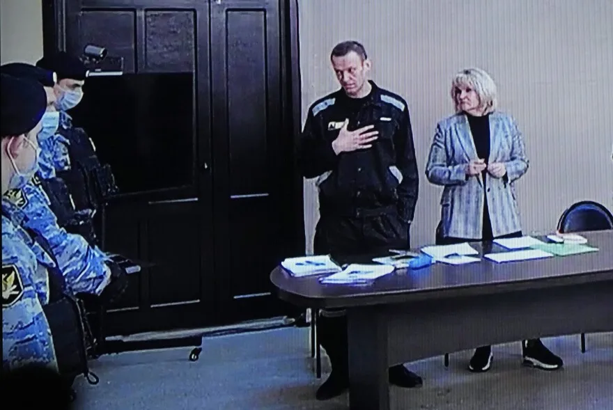 March 22, 2022: Russian opposition leader Alexei Navalny, centre, gestures via a video link provided by the Russian Federal Penitentiary Service, standing next to his layer and speaking with Penitentiary Service officers during a court session, in Pokrov.