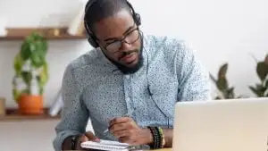 man in headphones writing notes in notebook watching webinar video course