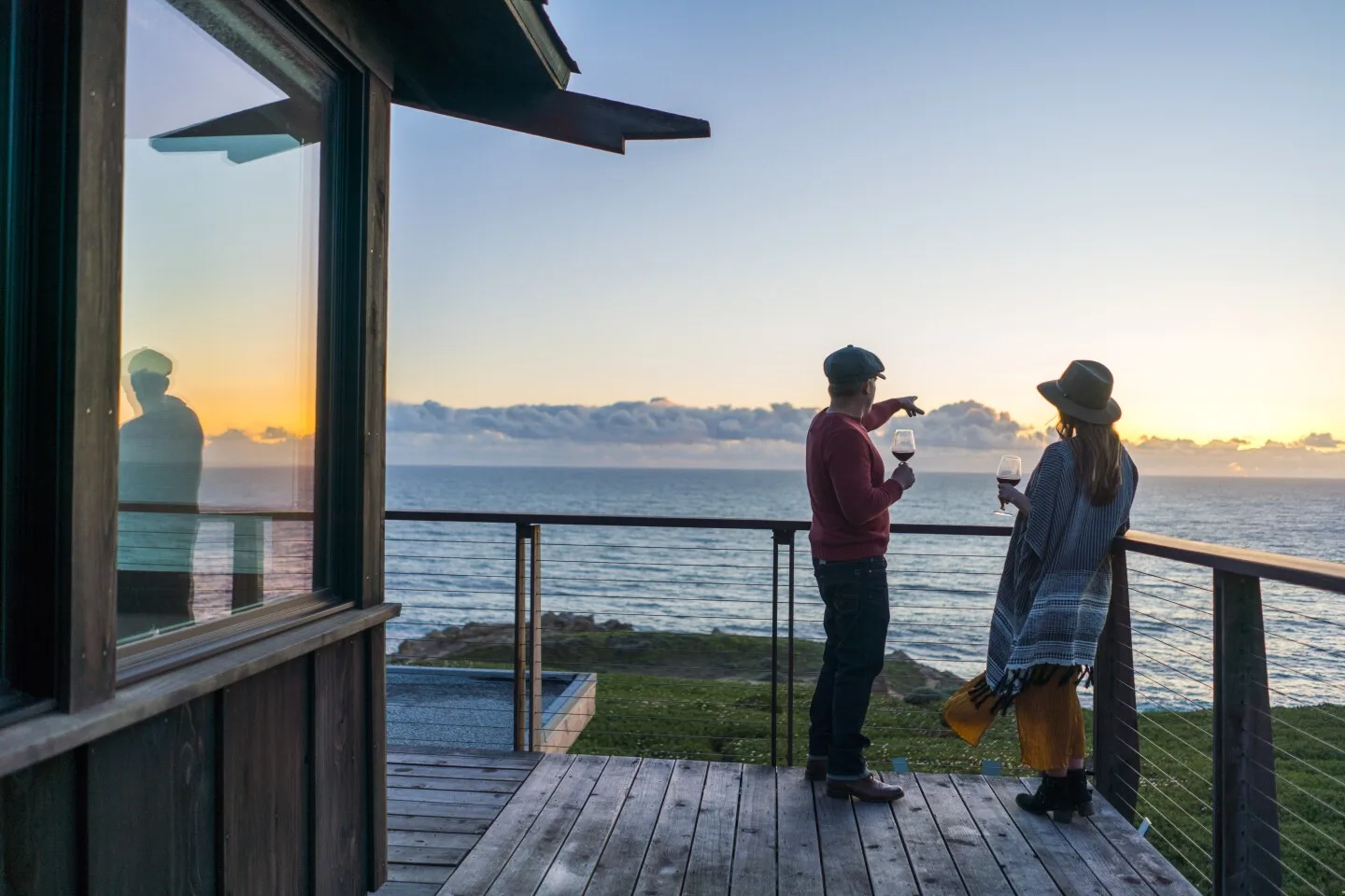 Two people drinking wine and viewing a sunset on a wooden porch overlooking the Sonoma coast