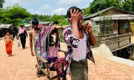 Two young men carry an older woman in a chair.