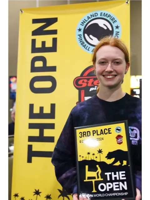 Emily Cosson holding a third place trophy in front of a yellow sign