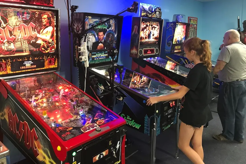 A young girl playing pinball next to a man