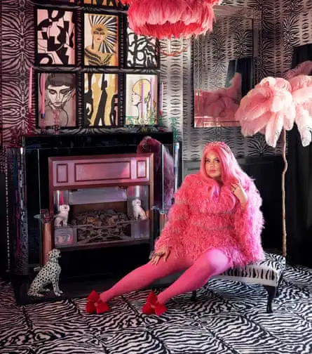 Siobhan Murphy wears a pink outfit, sort of imagine a shaggy dog kind of fur top, with jewelled ornaments. She has a pink wig and crown and huge red bow ties on her red shoes.