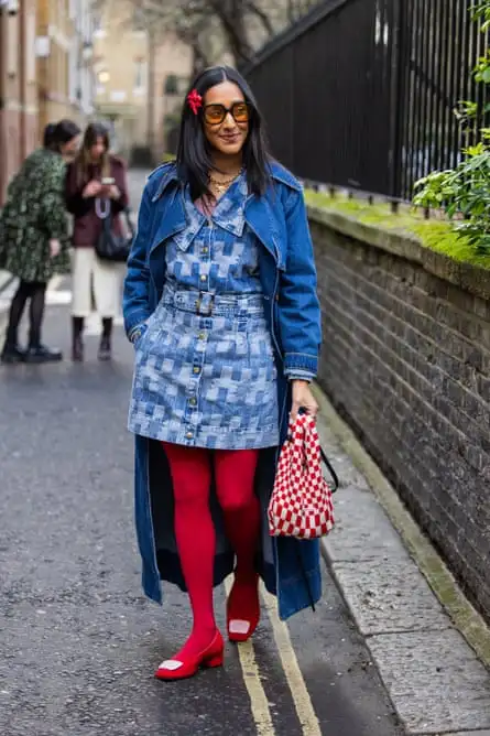 Street photo of Zeena wearing a mixed-blue denim skirt with darker blue denim jacket, red tights and red shoes with a white square on the toes. She is holding a red and white chequered bag.