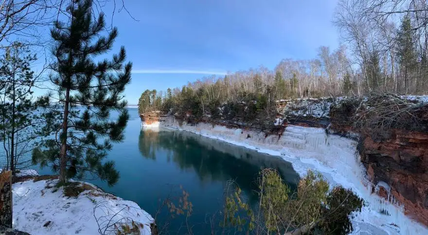 ice hangs in sheets on sandstone cliffs along a deep blue lake in wintertime