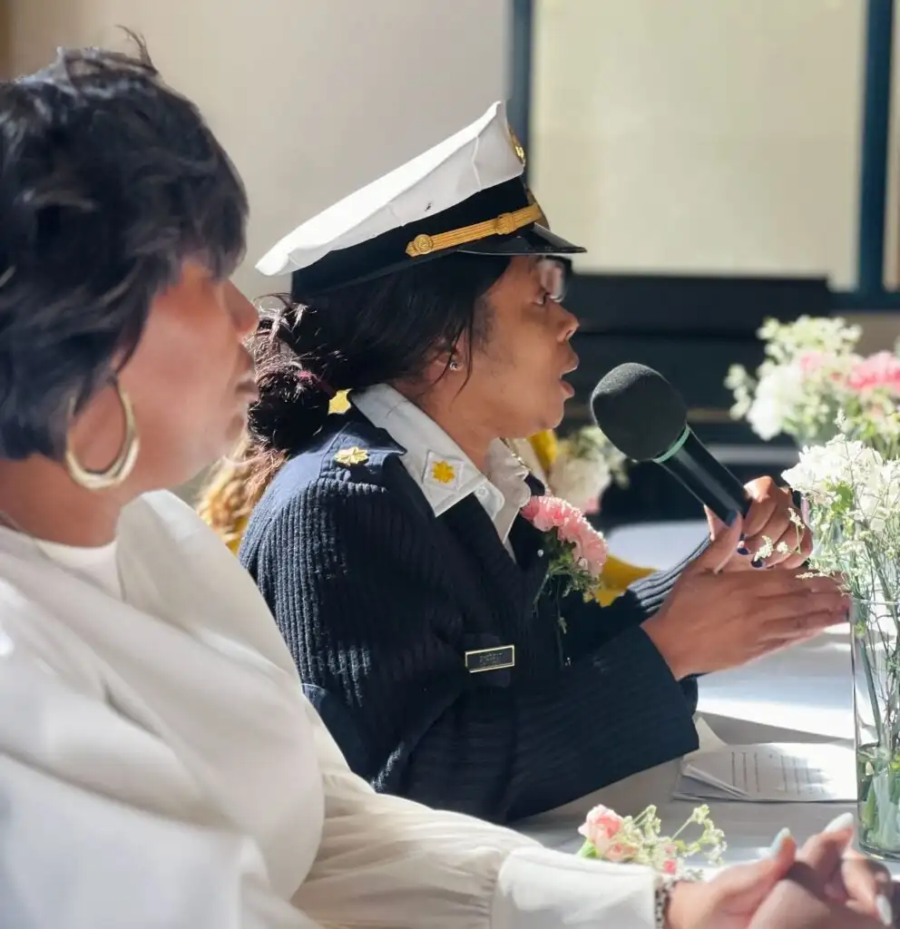 Farida Boyer watching as Lisa Forrest speaks into a microphone