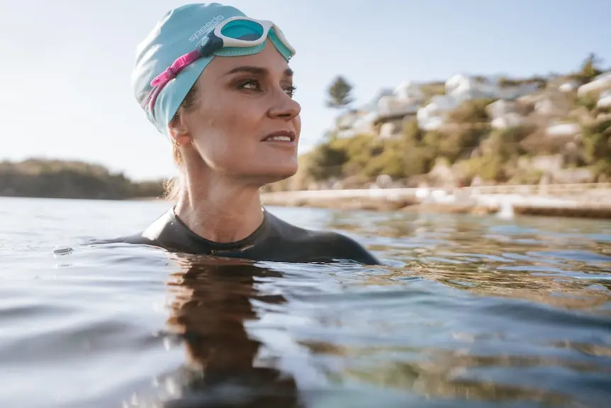 Julia Baird, who is wearing a blue swim cap and goggles submerged in the sea, looks back at the shore in warm morning sunlight