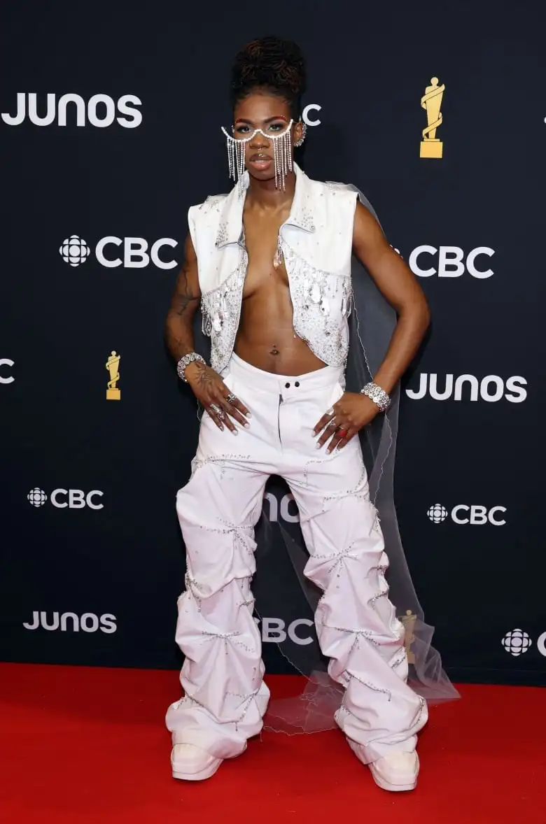 Haviah Mighty on the Juno Awards red carpet wearing a white, sparkly vest and pants accessorized with a glasses-like piece embellished with rhinestones.