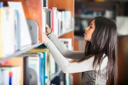 A dark-haired girl looking through books on a shelf in a library