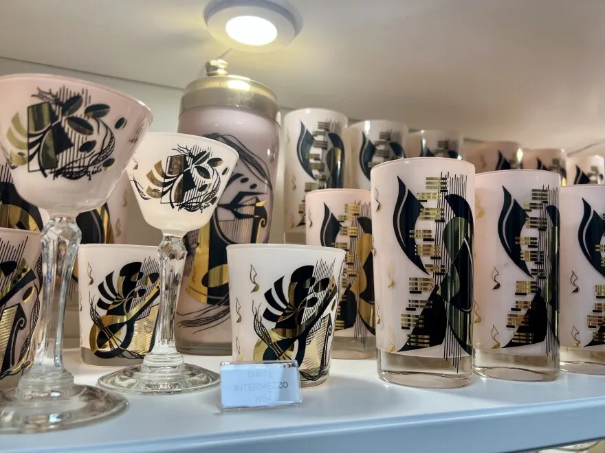 Original Gay Fad designed glassware with pink, black and gold designs sits in a cupboard.