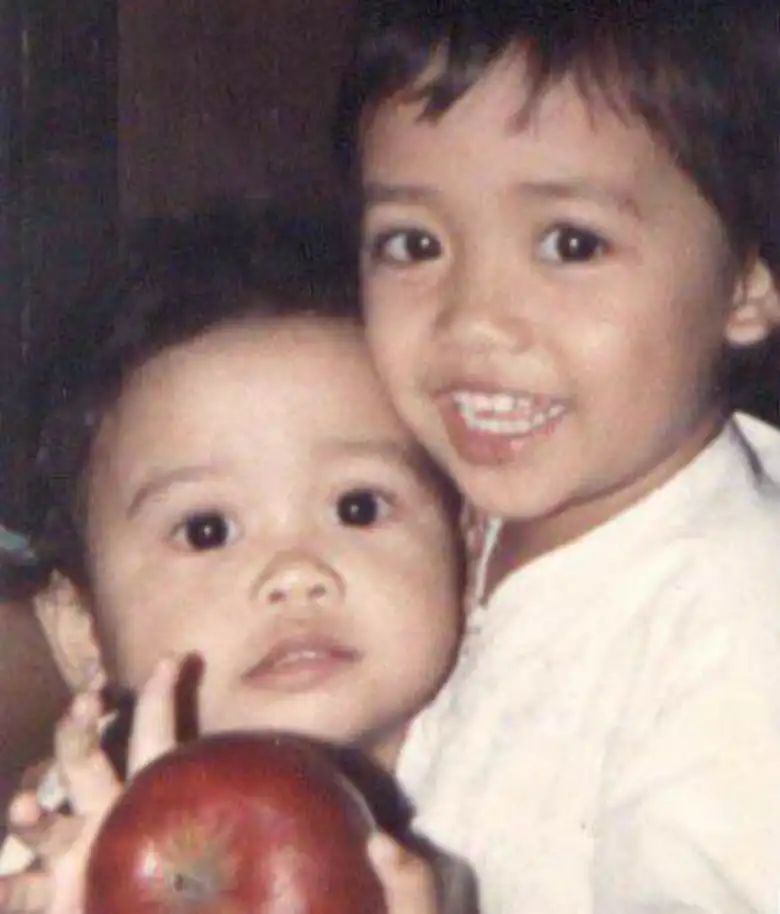 A photo of two infants. The one on the right holds a red apple.