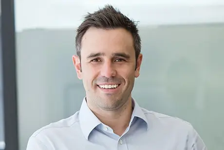 A man wearing a light coloured collared business shirt smiling.