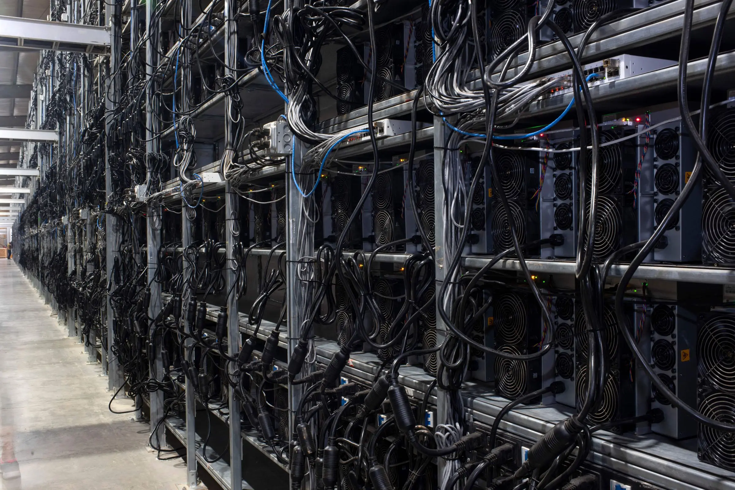 Racks of Bitcoin mining machines with wires hanging from them.