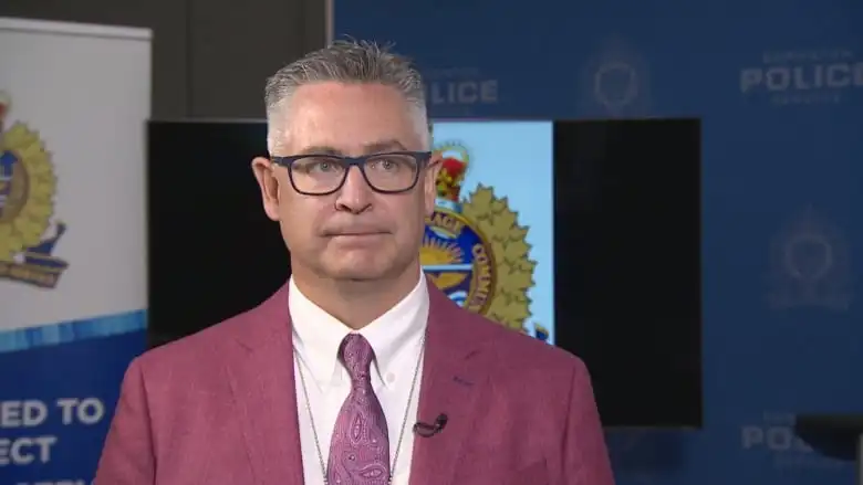 A man in front of the Edmonton Police's logo looks into the camera.