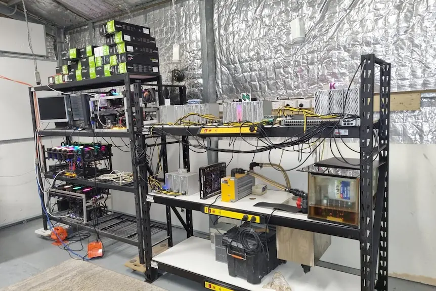 Two shelves in an insulated shed with electrical equipment, computers and cords.