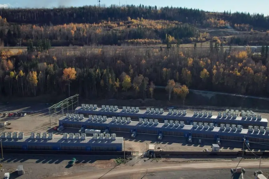 A bird's eye view of three long sheds in an isolated stretch of land on the side of a hill.