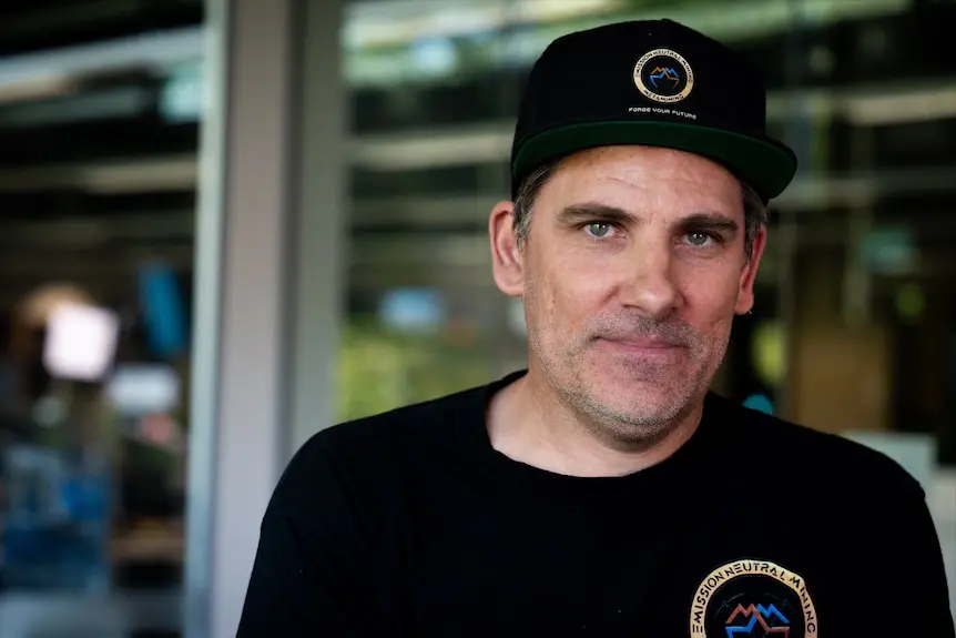 A man wearing a black tshirt and black cap in an office.