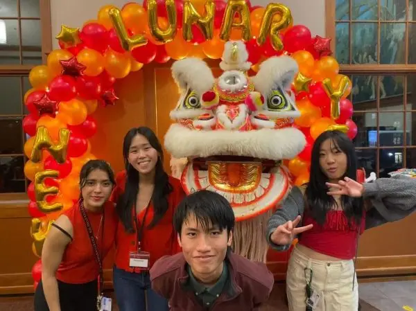 Emmeline Wendel with friends and a dragon costume next to a banner that says Happy Lunar New Year