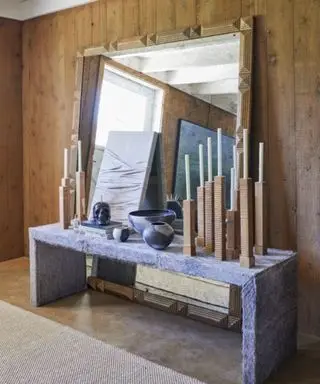 A console table with a large mirror resting behind and candlesticks layered on top