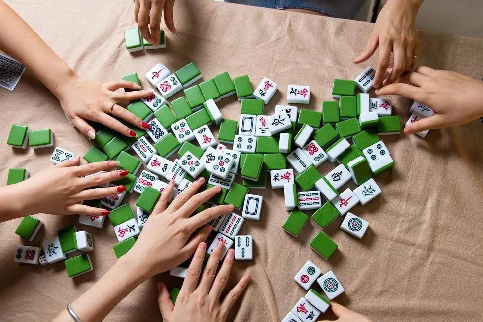 people mixing tiles while playing chinese board game mahjong at home