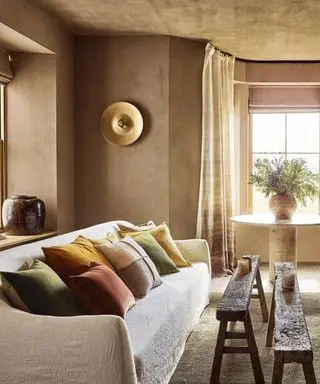 A living room with textured light brown walls, a sofa with colorful pillows and two small benches