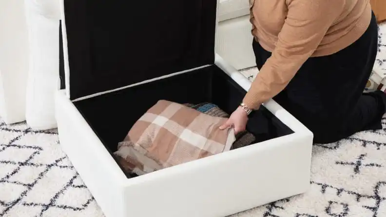 A person lifting up an ottoman to reveal the hidden storage.