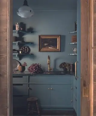 blue kitchen with brass fittings and art on walls and open shelves