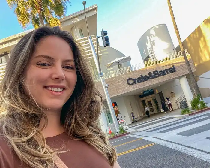 Selfie of the writer, wearing a brown T-shirt, in front of a Crate and Barrel store with palm trees in the background