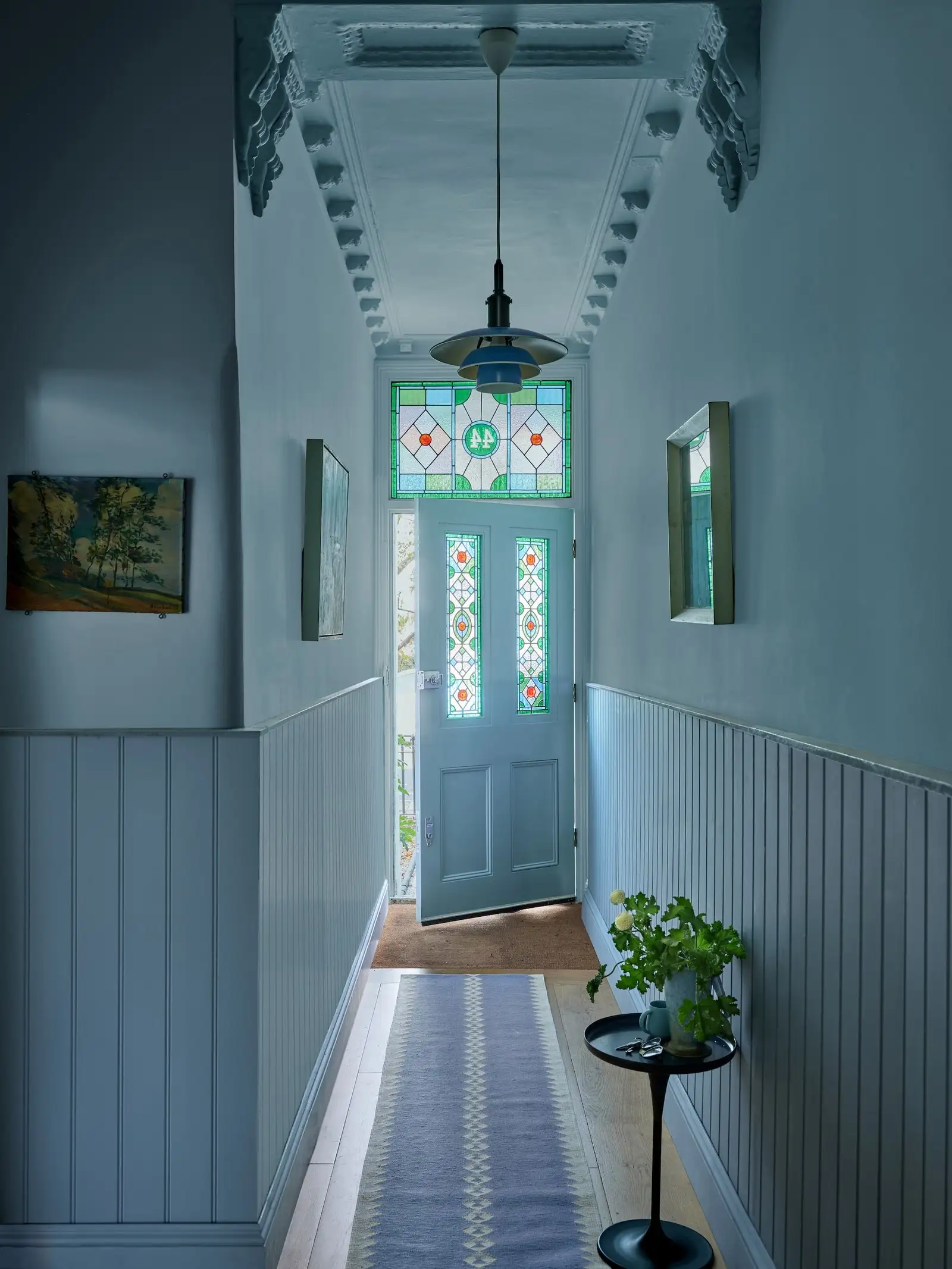 Blau gestrichener Hausflur mit Tür und Fenster mit Buntglas