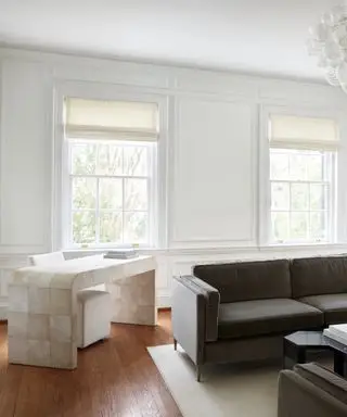 drapes vs blinds, minimalist living room with curved desk in left corner, mocha couches on right, hardwood floor, cream Roman blinds