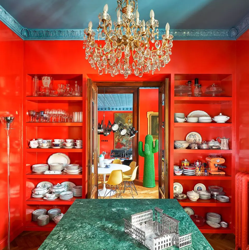 from the kitchen, a green marble countertop with built in shelves with dishware and glassware on either side of a door leading to a dining room with a large standing green cactus sculpture next to a table and chairs