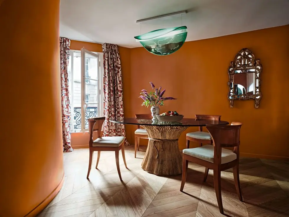 a dining are painted in a terra cotta planter color with a curving wall with a pedestal table and chairs, and a green glass light fixture overhead