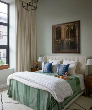 sage green bedroom with artwork on wall and blue accent cushions on bed