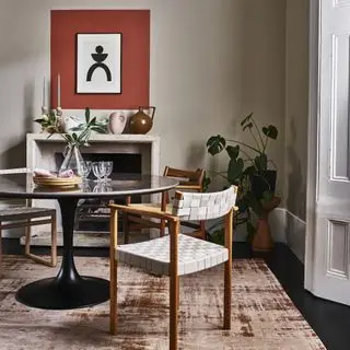 A dining room with a round dining table, woven chairs and a patterned rug