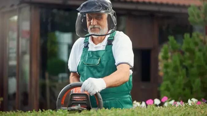 Front view of eldery man landscaping and taking care of plants in garden.