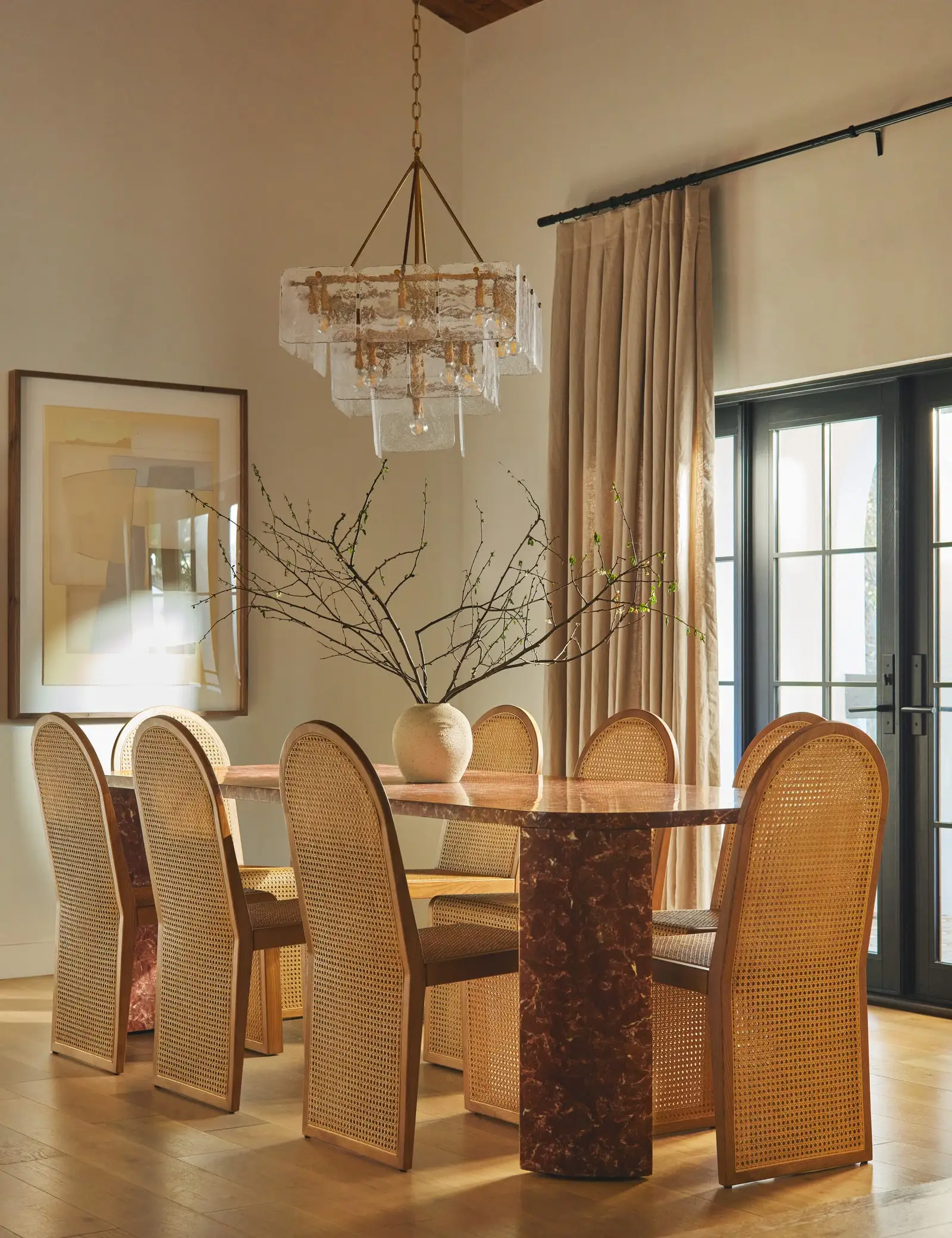 Marble dining table surrounded by high back cane chairs in a dining room with a chandelier above the table.