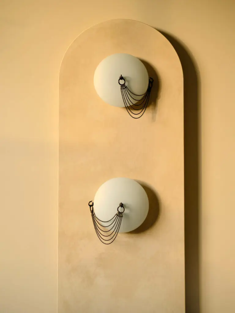 a wall sconce with two white lights featuring brass chains