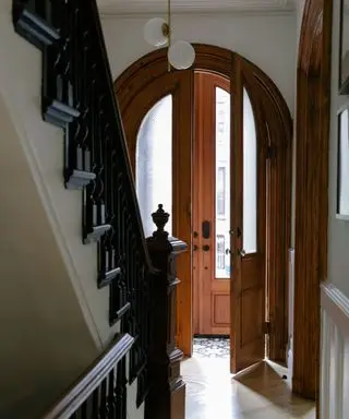 An arched wooden doorway and black and white staircase in a historic brownstone