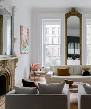 A white living room with a gold floor-to-ceiling mirror and an ornate cream fireplace