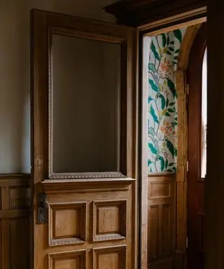 A carved wooden door leading to an entryway with green patterned wallpaper