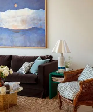 living room with white walls, dark brown sofa, blue artwork and white lamp