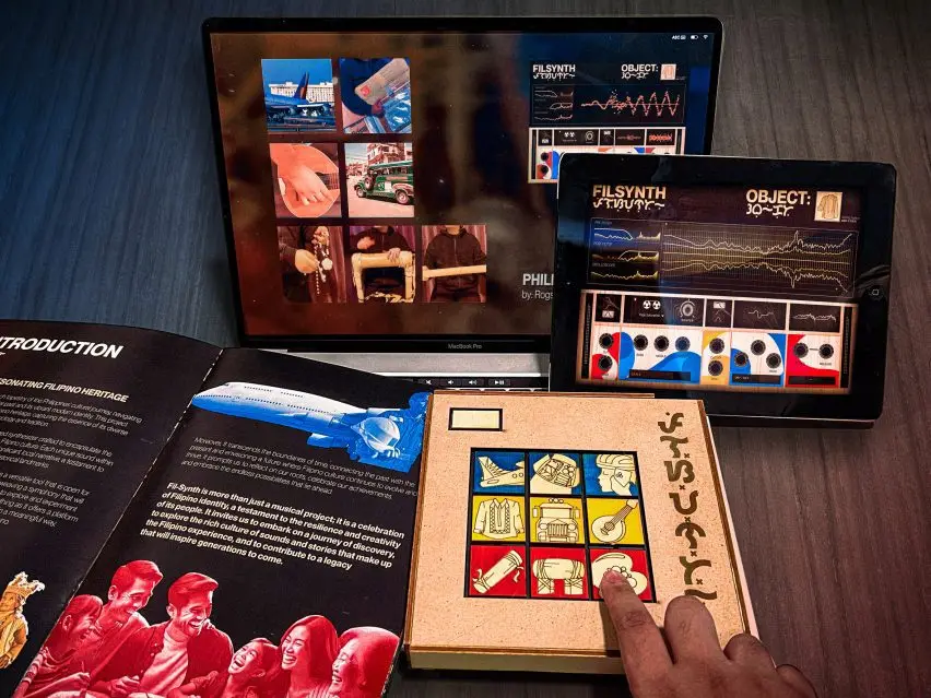 A photograph of a tablet, laptop, booklet and small box that display colours of red, blue and yellow. A person's finger is tracing an image on the box.