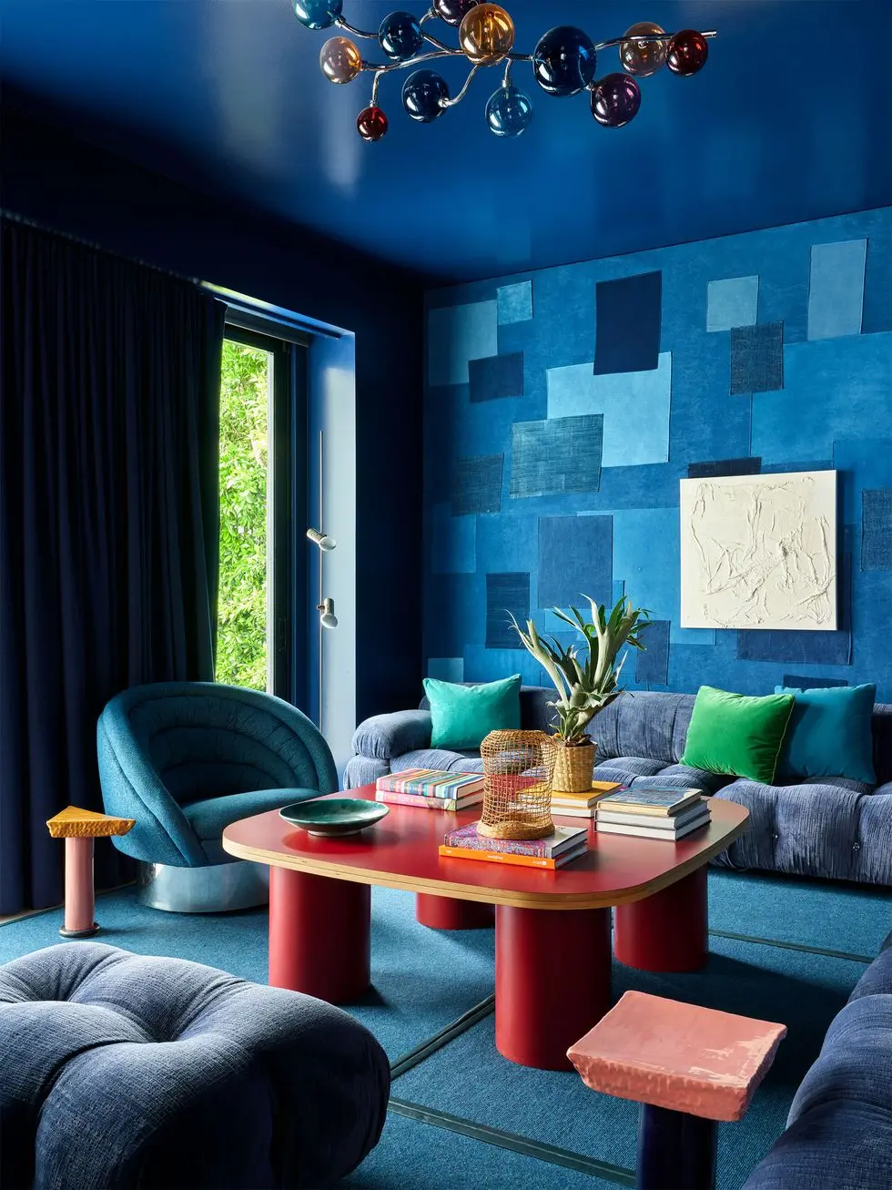 a multihue blue soft paneled room room with an oval red cocktail table and plush tufted chairs