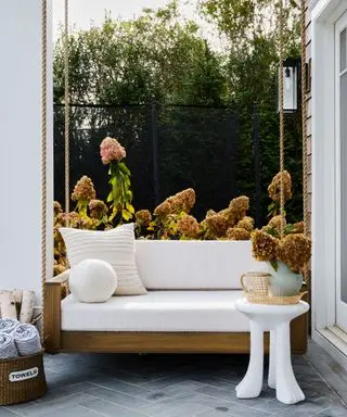 porch with white sofa, white cushions and white side table with garden flowers in the background