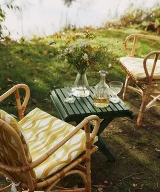 two outdoor chairs with yellow and white patterned upholstery and green side table with vase of flowers and drinks