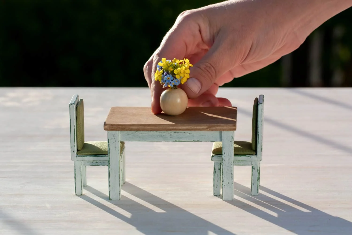 A hand decorating a wooden dining table with flowers in a vase, doll house furniture, home decoration or flower arrangement concept