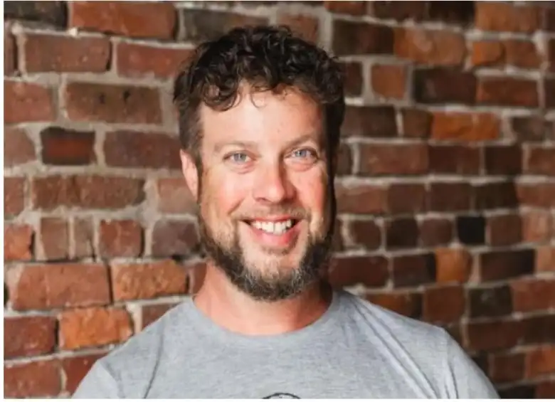 Man smiling at camera with a brick wall behind him.