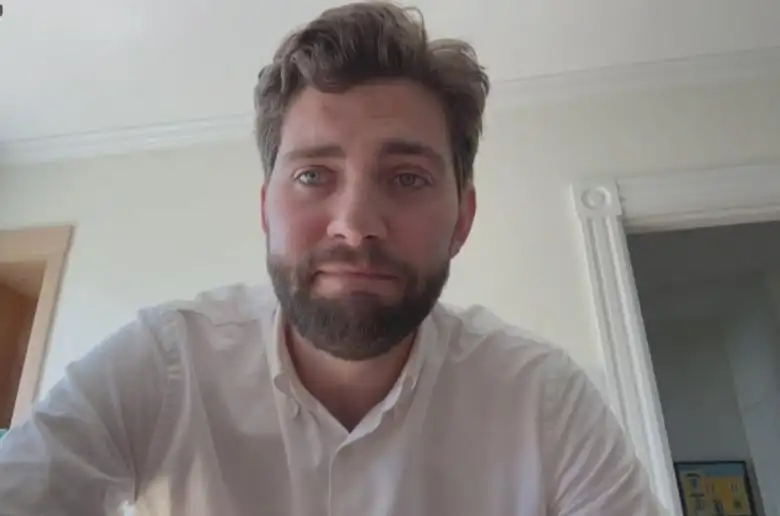 Man looking into a camera with a neutral expression during Zoom video call.