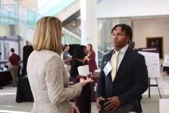 a photo of a young man in a suit speaking with a woman in a plaid blazer