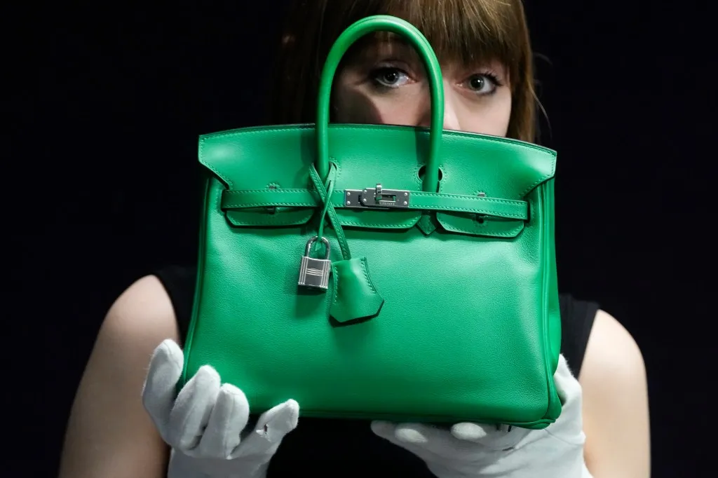 A Hermes Bambou Swift Leather Birkin 25 handbag displayed by a Bonhams employee at a live auction featuring luxurious bags and designs.